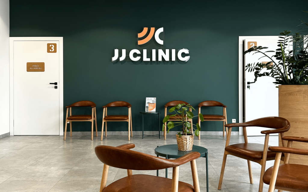Poczekalnia kliniki ortopedycznej JJClinic – zielona ściana z neonem logo oraz wygodna strefa oczekiwania dla pacjentów