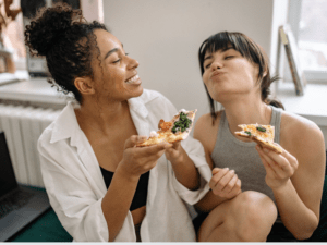 Dwie kobiety jedzą pizzę przy stole – przykład elastycznego podejścia do diety i zmiany nawyków