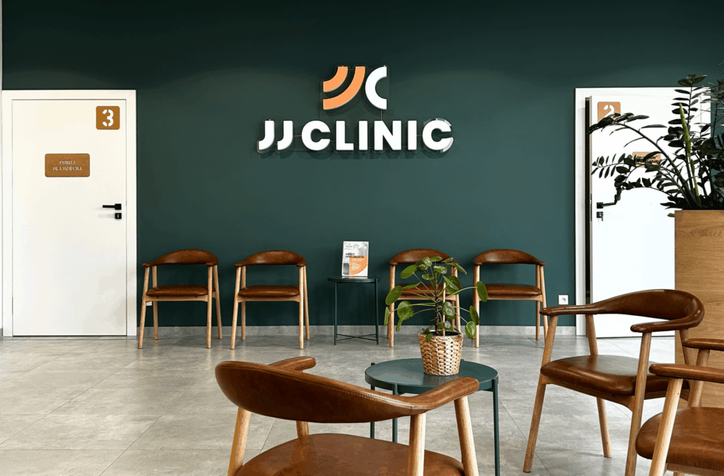 Poczekalnia kliniki ortopedycznej JJClinic – zielona ściana z neonem logo oraz wygodna strefa oczekiwania dla pacjentów