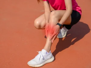 Biegaczka z kontuzją nogi kuca na bieżni lekkoatletycznej po treningu.
